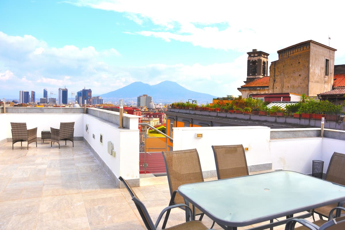 A rooftop terrace with a glass table and chairs, a view of a cityscape and a mountain in the background.