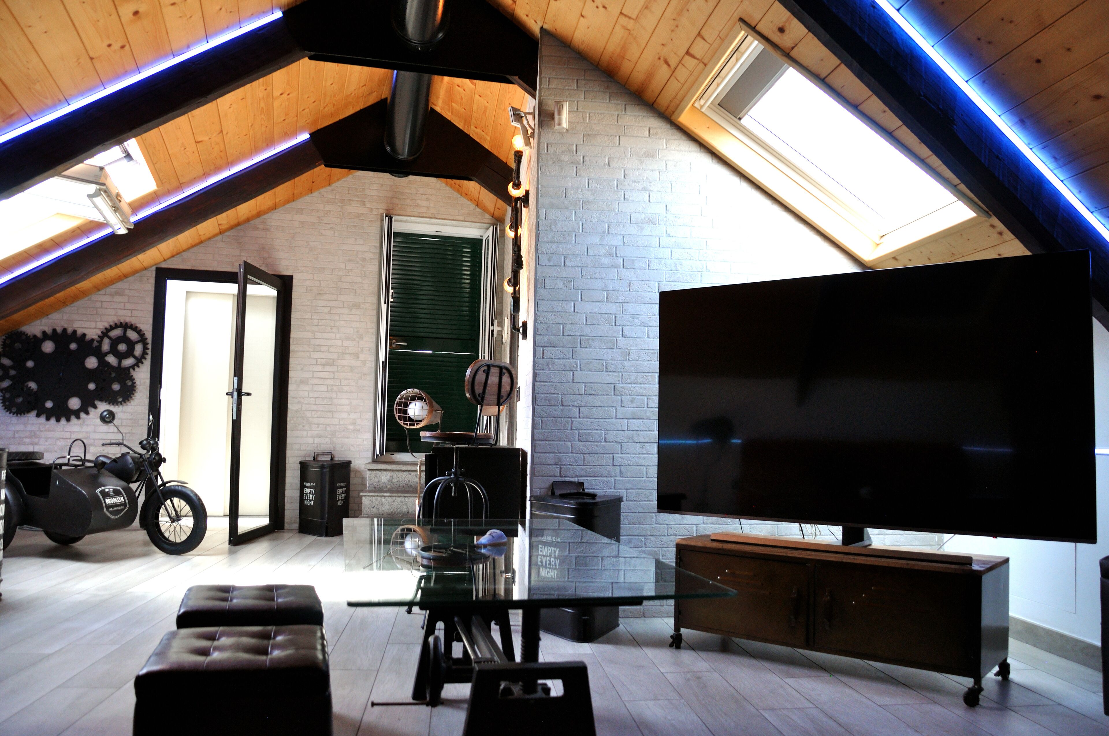 A loft-style room with a large flat-screen TV, a glass dining table, and a motorcycle with a sidecar.