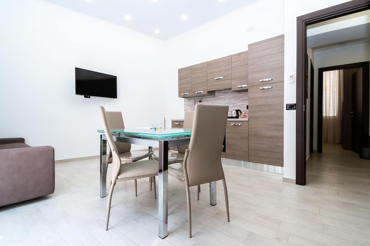 A modern dining area with a glass-top table, two chairs, and a flat-screen TV mounted on the wall.