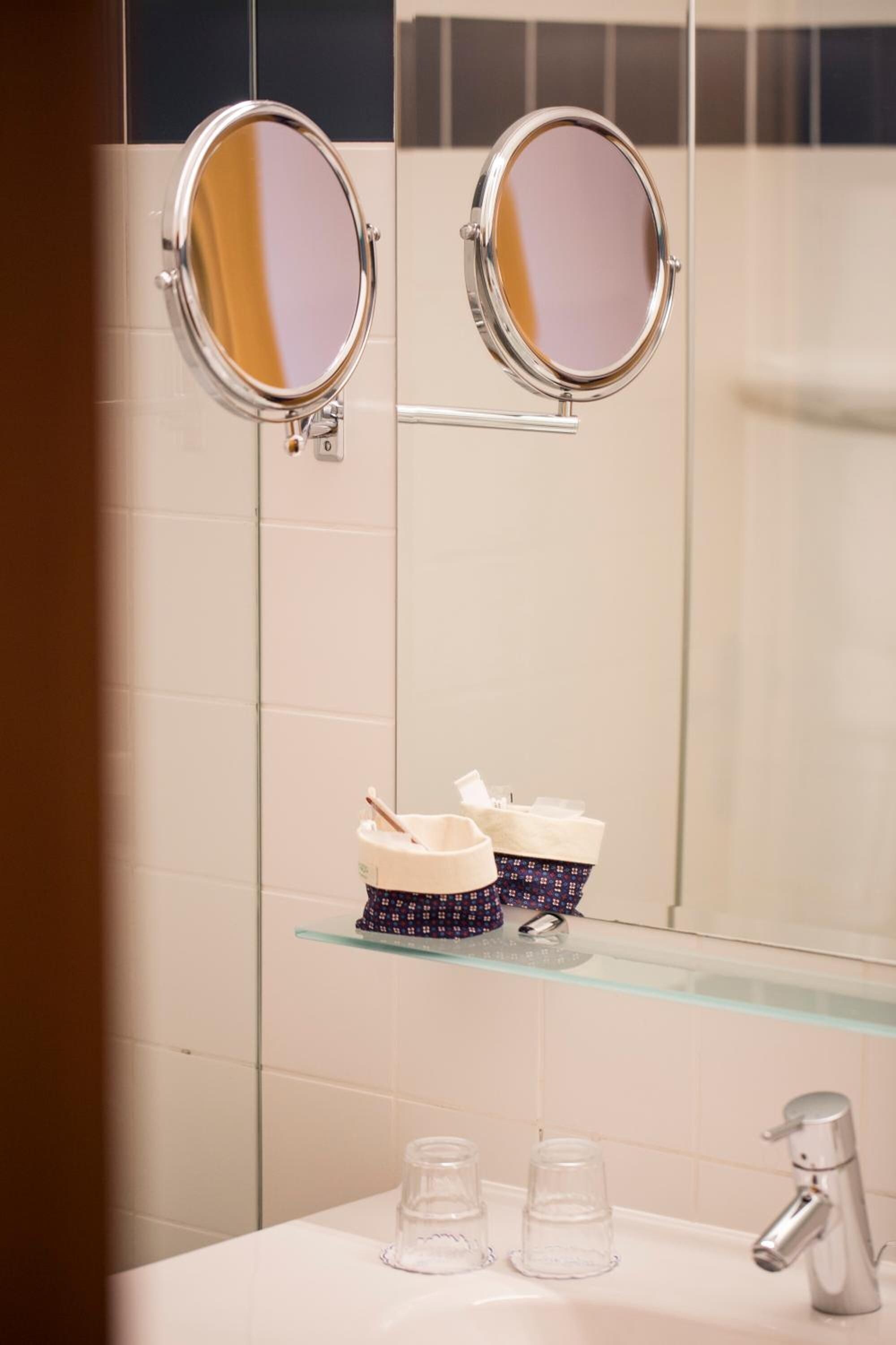 Un baño con dos espejos redondos colgados en la pared, un estante de vidrio con artículos de tocador y un lavamanos con grifo.