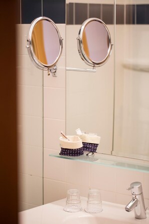 A bathroom with two round mirrors mounted on the wall, a glass shelf with toiletry items, and a sink with a faucet.