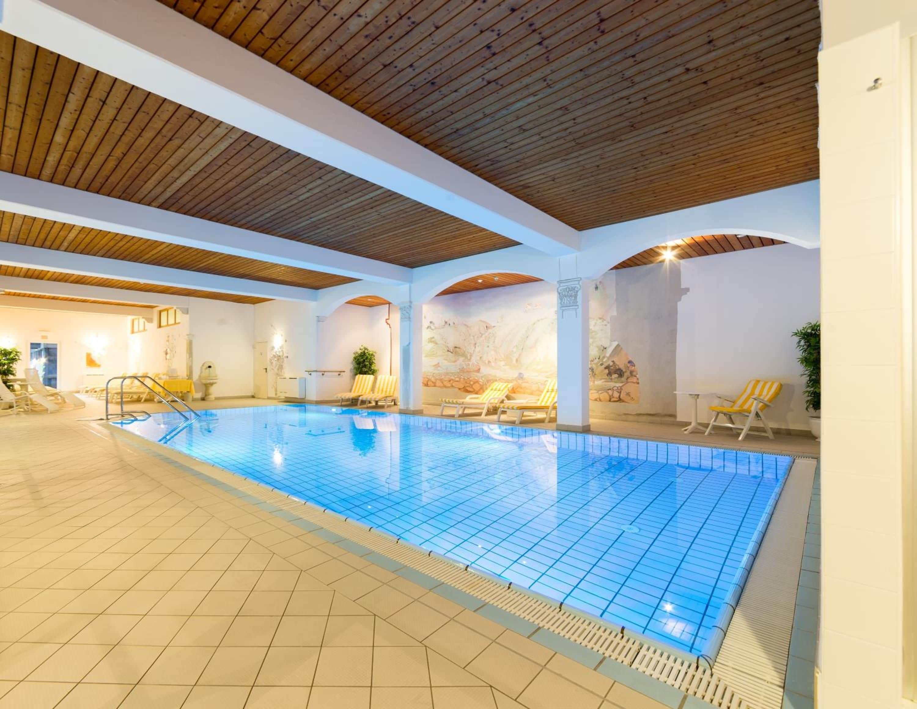 Ein überdachter Pool mit Fliesenboden, Liegestühlen und einer Holzzieldecke.