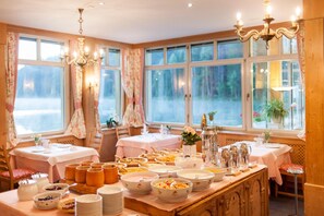 A dining area with multiple tables set for breakfast, featuring a variety of food items and utensils.