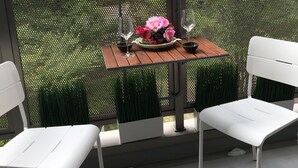 Un balcón con una mesa dispuesta para dos personas, adornado con un florero y dos copas de vino.