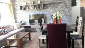 Una sala de estar moderna con pared de piedra, un televisor de pantalla plana, un sofá, una mesa de centro y un comedor con sillas y una mesa.