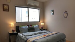 Un dormitorio con cama, dos mesitas de noche, una ventana y un equipo de aire acondicionado.