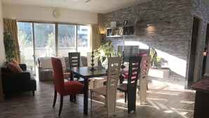 Un comedor moderno con un muro de acento de piedra, una mesa de comedor con sillas y un sofá con un cojín rojo.