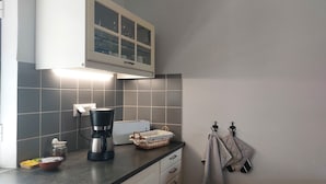 Une cuisine avec des carreaux gris, une machine à café, un grille-pain et un meuble avec des portes en verre.