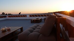 Une terrasse sur le toit dotée d’un espace salon avec des coussins, d’une table en bois avec des verres et une bougie, et d’une rambarde ornée d’un motif en zigzag.