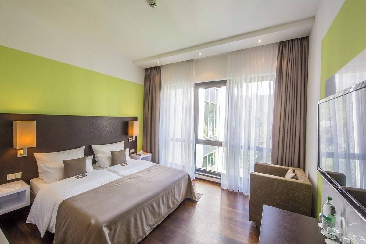 A hotel room with a bed, a chair, a TV, and a window with curtains.