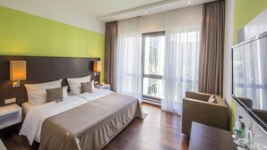 Habitación de hotel con cama, una silla, televisor y ventana con cortinas.