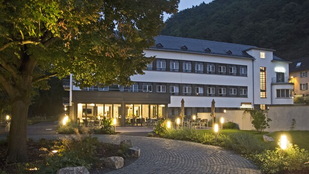 Un hotel con patio empedrado, mobiliario exterior y montañas al fondo.