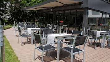 An outdoor dining area with tables and chairs, a covered patio, and a view of the building's exterior.