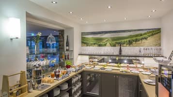A breakfast bar with a variety of food and drink options, a wine bottle, and a scenic vineyard painting on the wall.