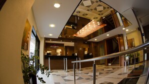 Un moderno vestíbulo de hotel con mostrador de recepción, una escalera y una lámpara decorativa.