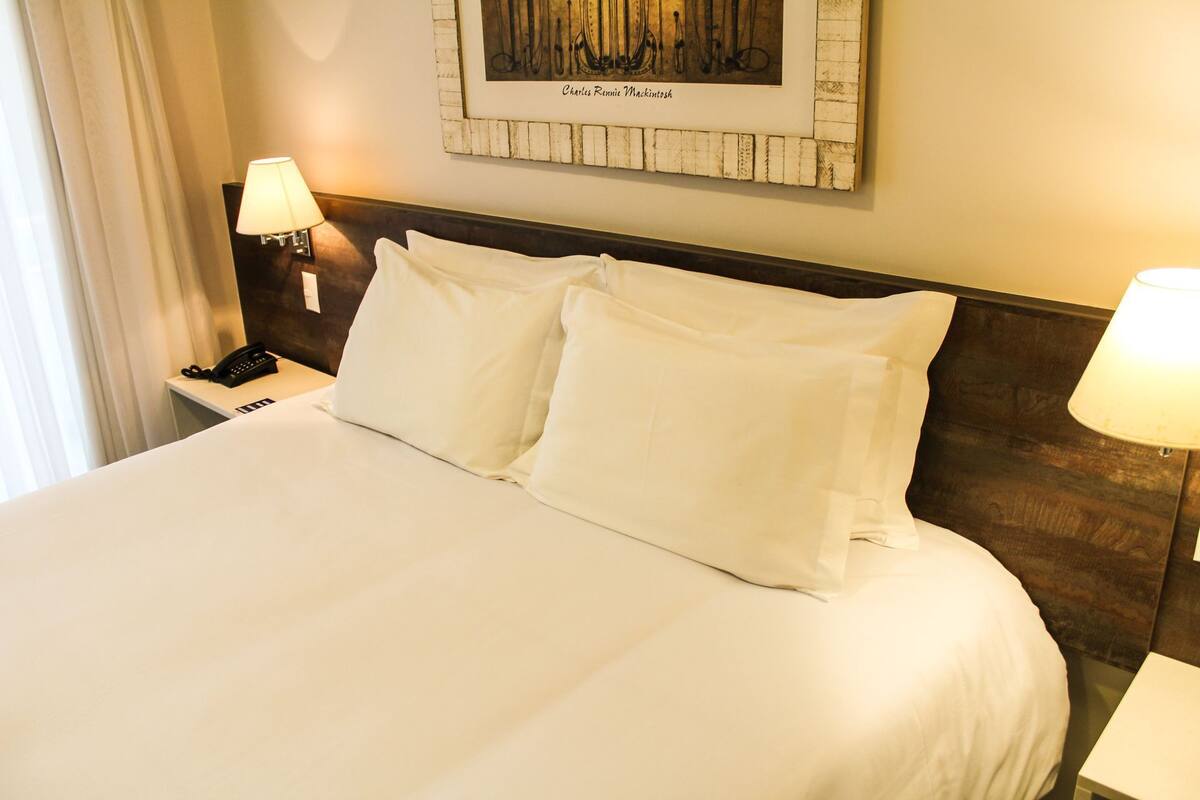 A hotel room with a large bed, two bedside lamps, a framed artwork on the wall, and a telephone on the nightstand.