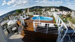 Un área de piscina en la azotea con terraza de madera, sillas de descanso y barandilla de cristal.