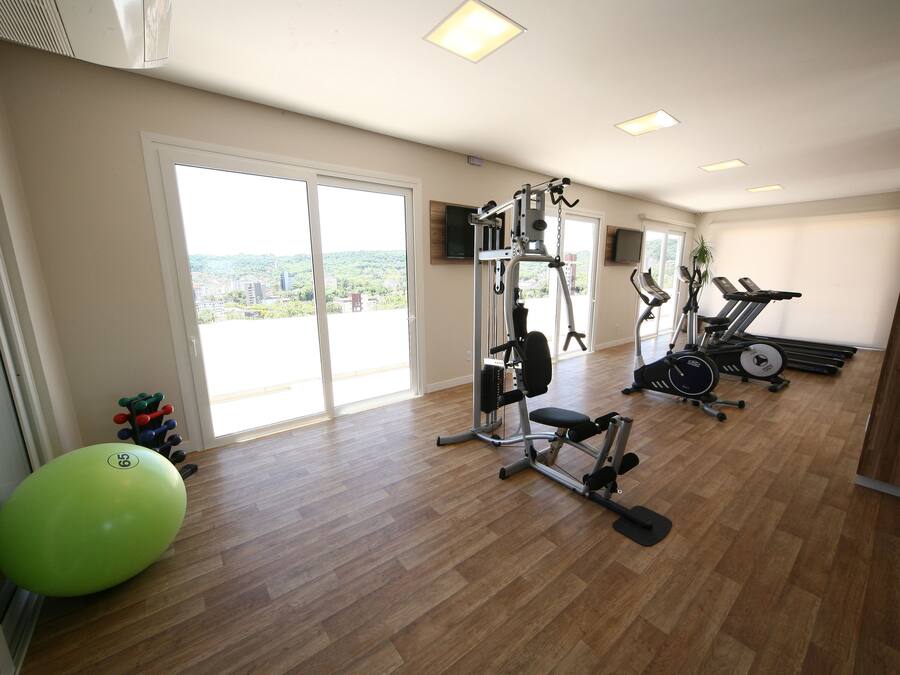 Un gimnasio con equipo de ejercicio, una pelota de entrenamiento verde y grandes ventanales con vistas.