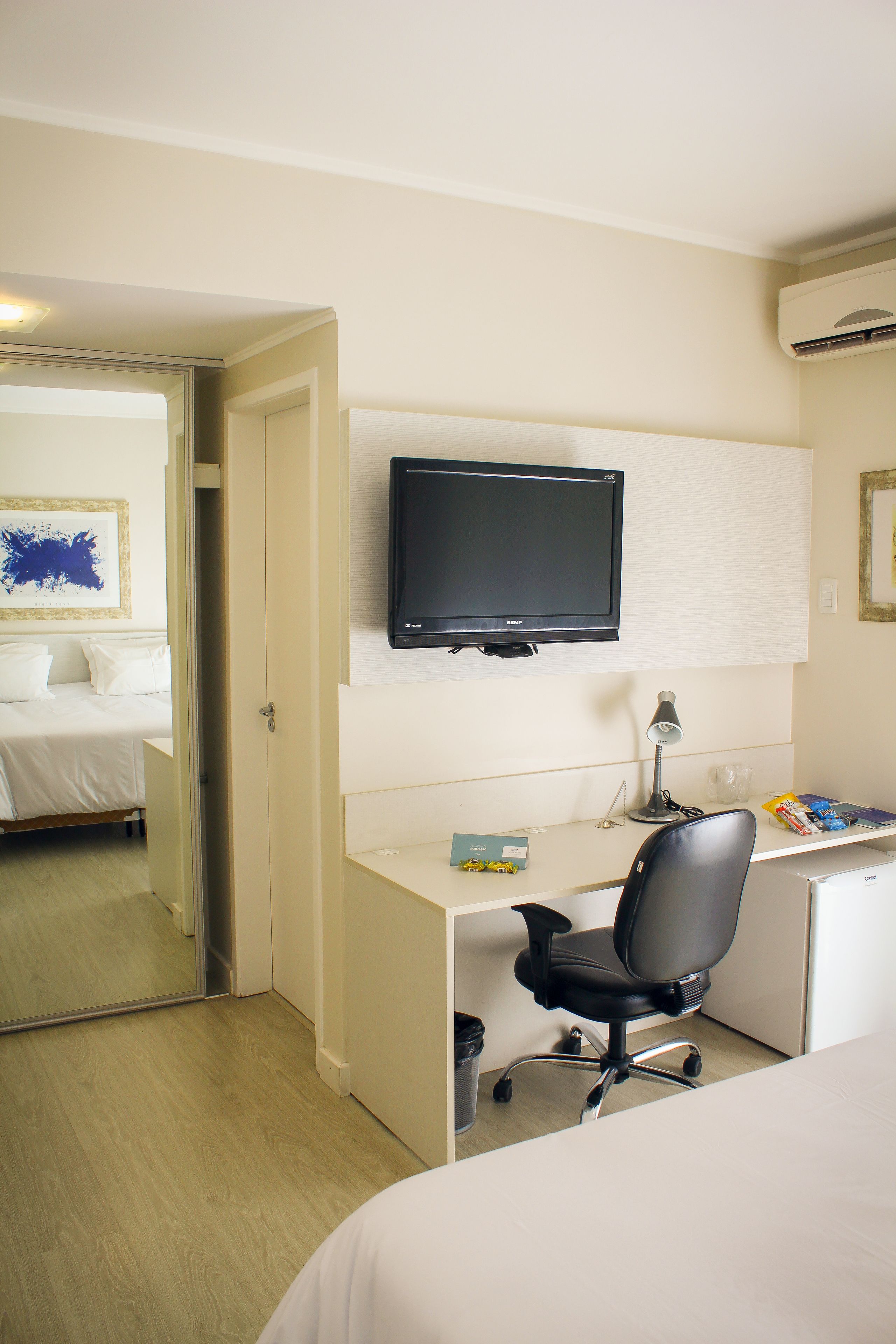 A hotel room with a bed, a desk with a chair, a television, and a small desk lamp.