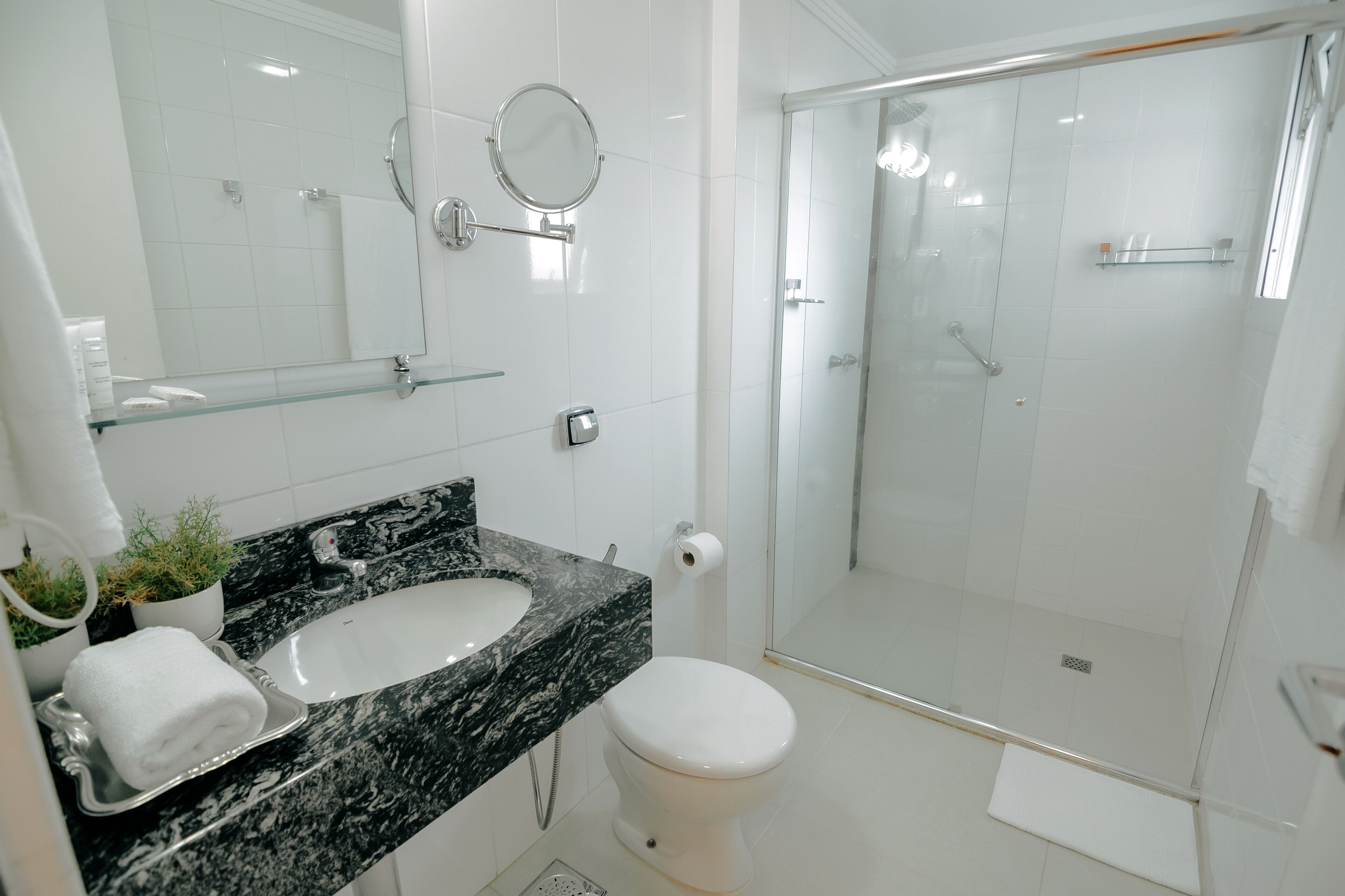 A modern bathroom with a marble sink, a toilet, a glass-enclosed shower, and a mirror with a round frame.