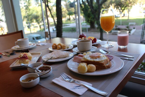 Una mesa de desayuno con diversos platos, entre ellos tostadas, fruta y un vaso de jugo de naranja.