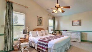 Un dormitorio con una cama grande, ventilador de techo, cómoda y ventana con cortinas.