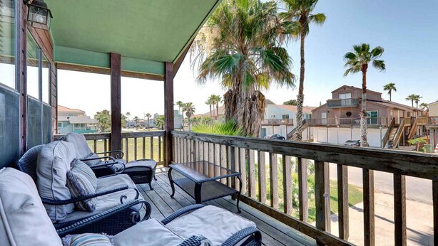 Un espacio de estar al aire libre cubierto con mobiliario de mimbre y vistas a palmeras y casas vecinas.