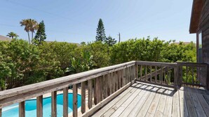 Una terraza de madera con piscina, rodeada de exuberante vegetación y árboles.