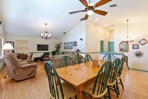 A spacious living room with a wooden dining table, green chairs, a beige sofa, and a ceiling fan. - Acapulco Villa South Padre Island (South Padre Island)