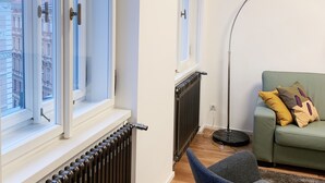 Ein modernes Wohnzimmer mit Heizkörper, einer Couch mit Kissen, einem Sessel und einer Stehlampe.
