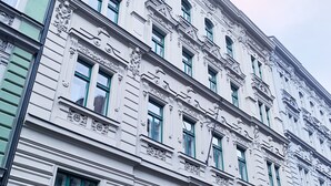 Ein mehrgeschossiges Gebäude mit klassizistischen architektonischen Details, darunter aufwendige Schnitzereien und Fenster mit grünen Rahmen.