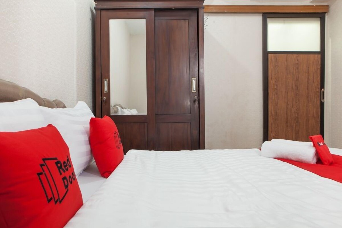 A hotel room with a bed, red pillows, a wardrobe, and a door.