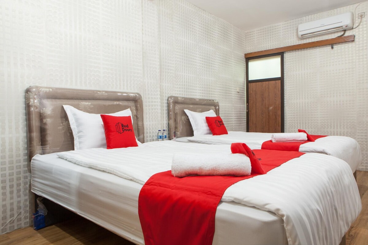 A hotel room with two beds, each with white bedding and red accents, and a wooden door.