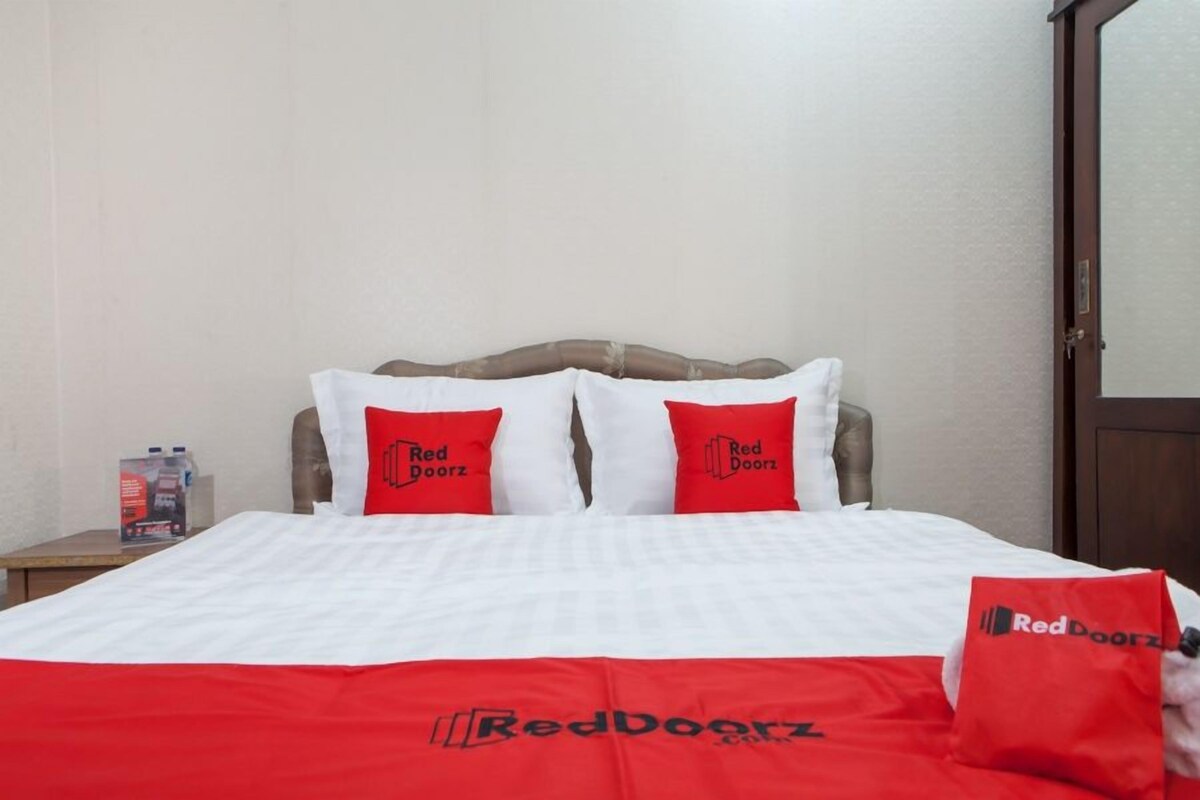 A hotel room with a bed, two pillows with 'Red Doorz' branding, a nightstand with a bottle, and a door with a mirror.
