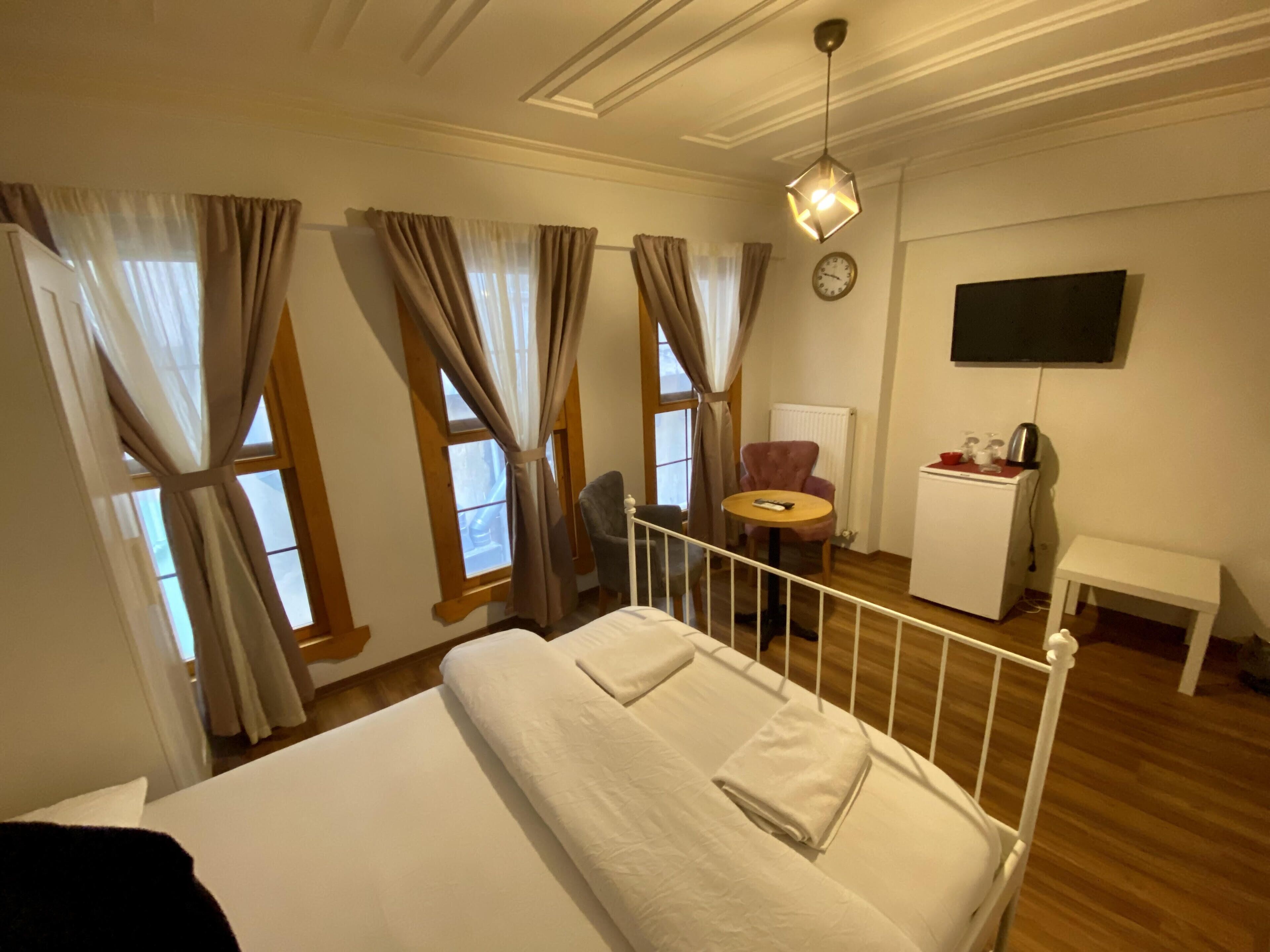 A hotel room with a bed, a desk, a chair, a TV, and a window with curtains.