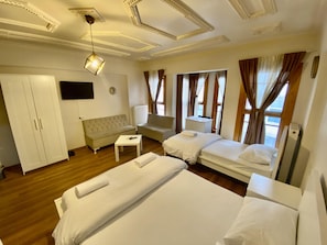 Une chambre d’hôtel avec deux lits, un canapé, une petite table, une télévision et une armoire.