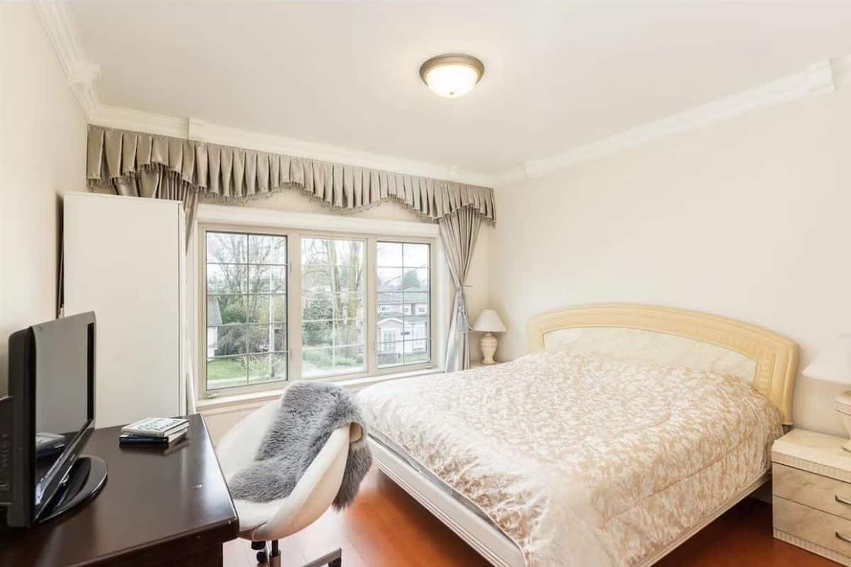 Une chambre à coucher avec un lit, un bureau avec un ordinateur, une chaise, une fenêtre avec des rideaux et une table de chevet avec une lampe.
