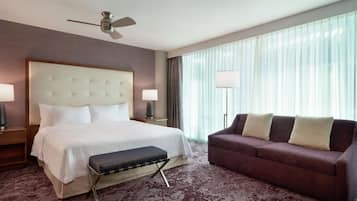 A hotel room with a large bed, a sofa, a ceiling fan, and a large window with curtains.