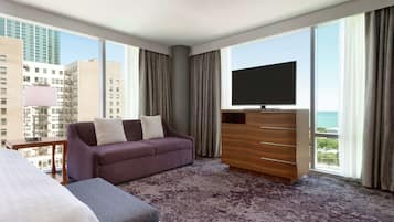 A hotel room with a large window, a sofa, a TV, and a bed.
