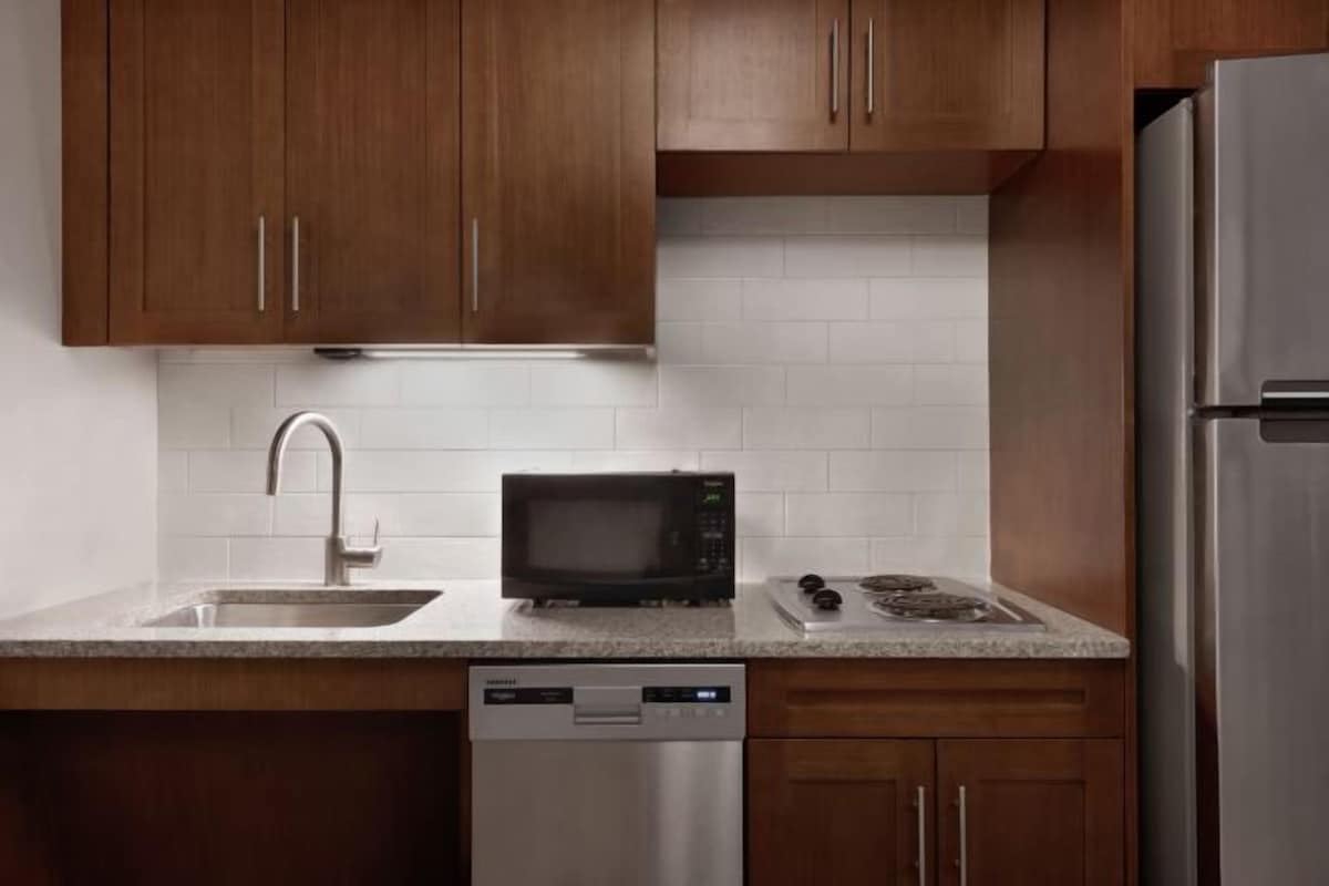 Una cocina con armarios de madera, un refrigerador de acero inoxidable, un microondas, un lavavajillas y una encimera de granito.