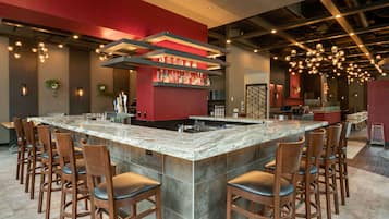 Zona de bar moderna con una isla grande de mármol, varios taburetes y una pared decorada en rojo.