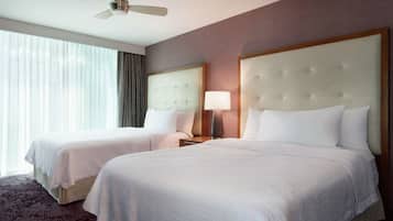 A hotel room with two beds, a ceiling fan, a large window with curtains, and a carpeted floor.