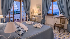 Ein Schlafzimmer mit Bett, Schreibtisch, Stuhl, einer Deckenleuchte und Blick ins Freie.