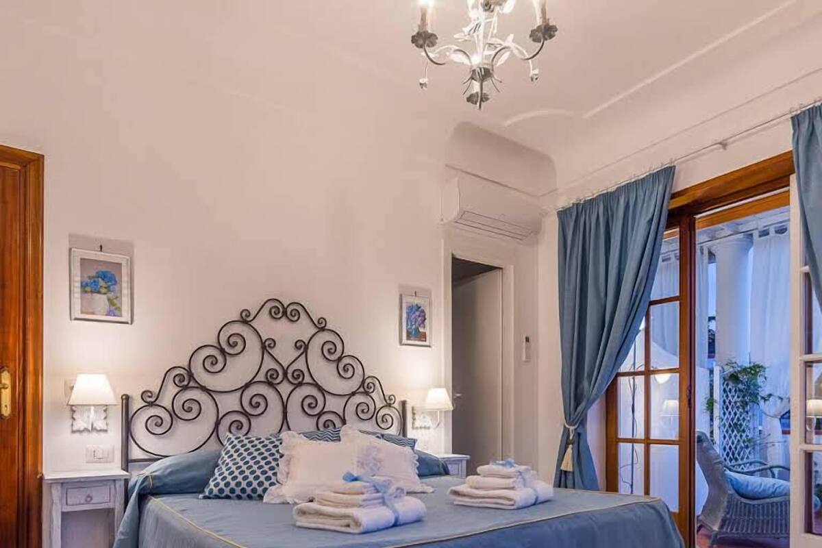 A bedroom with a bed, a chandelier, a door leading to a balcony, and a patterned floor.