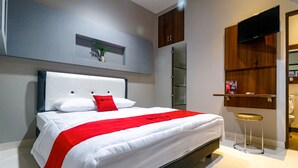 Ein modernes Hotelzimmer mit einem großen Bett, einem kleinen Hocker, einem an der Wand befestigten Fernseher und einem Regal mit einer Pflanze.