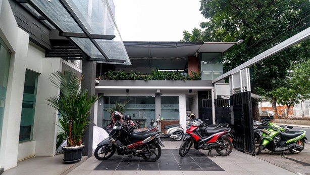 Ein modernes Gebäude mit überdachter Eingangspartie, ein Motorrad davor und ein Blumentopf daneben.