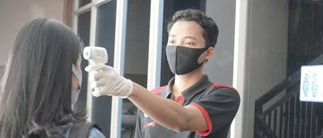 A person wearing a black shirt with red trim, holding a device for temperature screening.