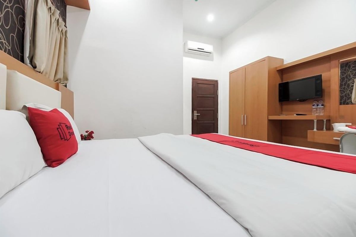 Une chambre d’hôtel avec un lit, un plaid rouge, une télévision et une armoire.