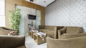 A living room with brown sofas, a coffee table, a TV, and a large plant. - RedDoorz near Mall Panakkukang 3 (Makassar)