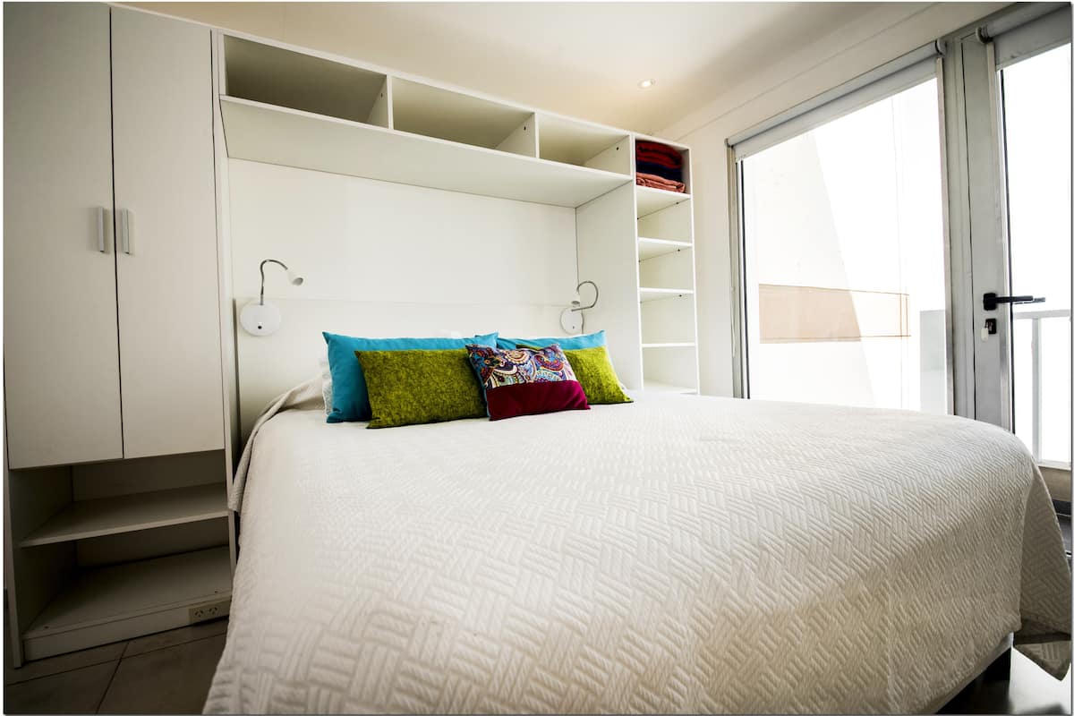 A bedroom with a large bed, built-in shelving, and a sliding glass door to the outside.